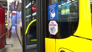An einem gelben Linienbus kleben Hinweisschilder zu Masken und Filtern.