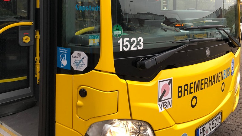 An einem gelben Linienbus kleben Hinweisschilder zu Masken und Filtern.