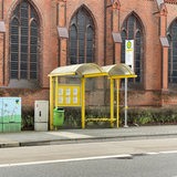 Eine menschenleere Bushaltestelle steht vor einer Kirche.