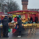 Auf einem Platz zwischen Gebäuden stehen Marktstände und vereinzelt Personen.