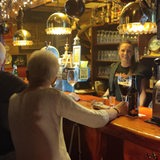Mehrere Personen sitzen an einer Theke, dahinter steht eine Frau.