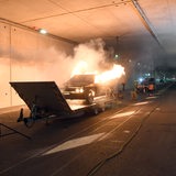 Eine Pkw-Attrappe steht in einem Tunnel in Flammen, drumherum stehen Feuerwehrleute.