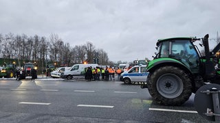 Protestierende Landwirte, Traktoren und ein Polizeiwagen stehen auf einer breiten Straße.