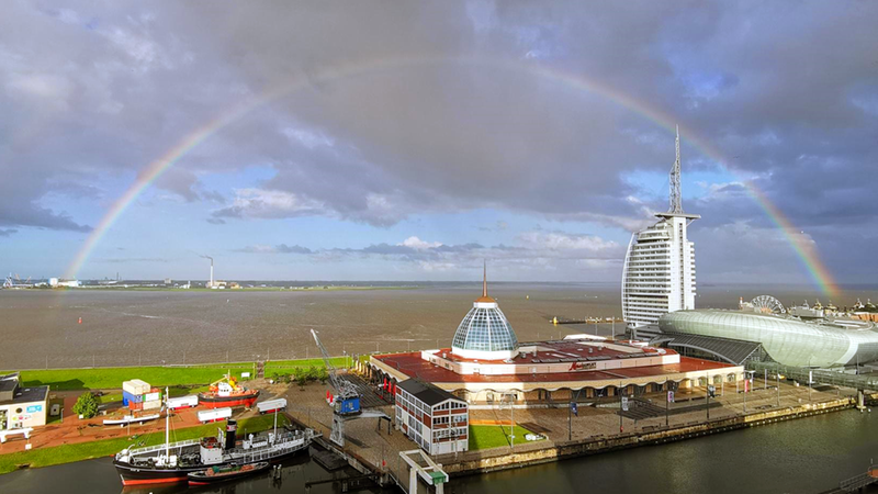 Ein Regenbogen steht über Gebäuden und Wasser.