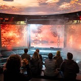 Museumsmitarbeiter und andere Personen sitzen auf der Erlebnisplattform während einer Besichtigung der Ausstellung zum Thema Wetterextreme im Klimahaus in Bremerhaven.