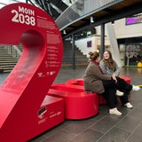 Zwei Personen sitzen auf einer roten Installation in einer Halle.