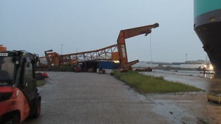 Ein umgestürzter Kran liegt in Bremerhaven am Hafen auf dem Ufer.