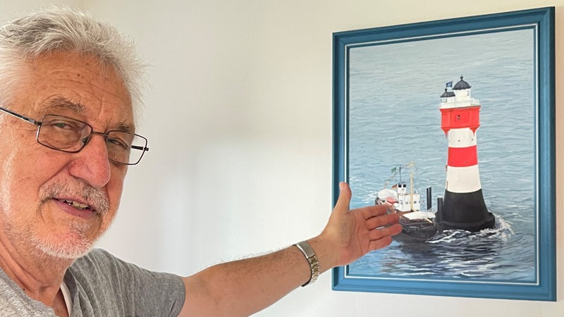 Ein Mann zeigt mit der Hand auf ein Gemälde eines Leuchtturms.
