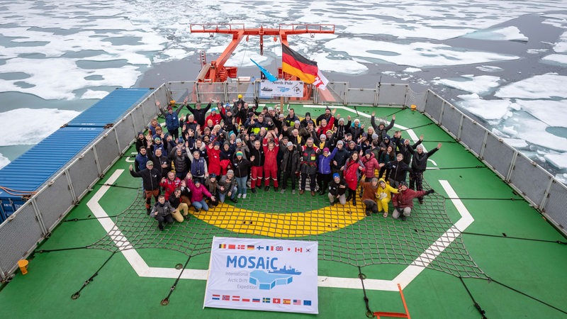 Eine Gruppe Personen steht auf einem Schiff im Eis und jubelt.