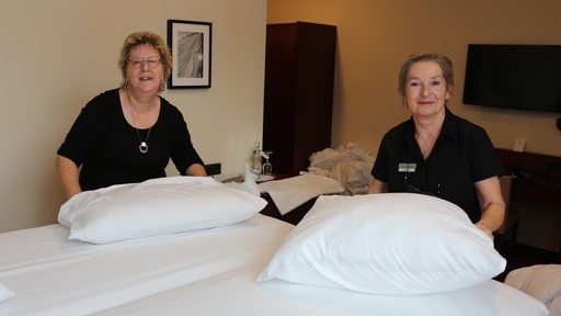 Zwei Frauen stehen an einem Hotelbett und haben Kopfkissen in der Hand.