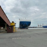 Ein blau-weißes Schiff liegt an einem Kai in einem Hafengebiet.