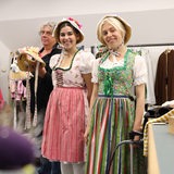 Zwei Frauen in bunten Kleidern stehen neben einem Mann in einer Garderobe.