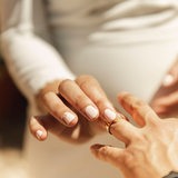 Eine Frau schiebt einen Ehering über den Ringfinger eines Mannes.