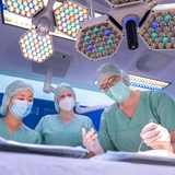 Drei Ärzte beugen sich in einem Operationssaal über einen OP-Tisch.