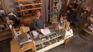 Eine junge Frau steht zwischen Lebensmittel-Regalen am Tresen eines Geschäfts.
