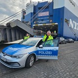 Zwei Wasserschutzpolizisten steigen vor einem im Hafen liegenden Frachter aus ihrem Auto.