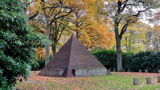 Eine große Pyramide aus Klinkersteinen steht neben Grabsteinen auf einem Friedhof im Herbst