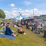 Menschen sitzen am Deich, Buden und Zelte sind an der Weser aufgebaut.