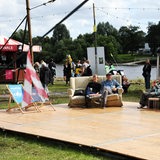 Auf einer Holzbühne neben der Weser sitzen Menschen auf Sofas.