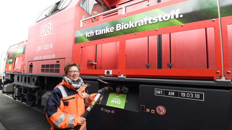 Eine Frau steht mit einem Zahpfhahn an einer Lokomotive.