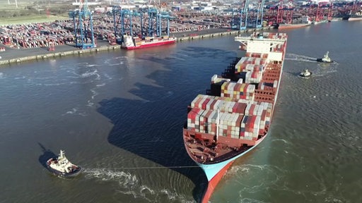 Ein voll beladenes Schiff mit Containern vor einem Hafen.