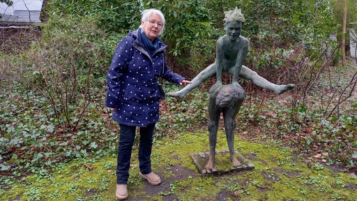 Eine Frau steht neben einer Skulptur.