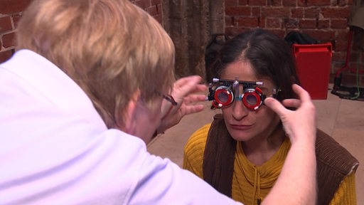 Eine Optikerin beugt sich zu einer Person, die eine Sehtest-Brille auf hat