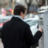 Ein Mann zieht an einem Parkscheinautomaten einen Parkschein.
