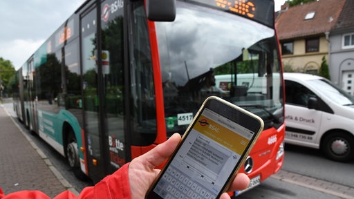 Eine junge Frau hält in Bremen ihr Smartphone vor einem Bus der BSAG. 