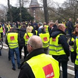 Menschen mit gelben Warnwesten stehen in der Bremer Innenstadt, im Hintergrund die Windmühle am Wall.