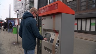 Ein Mann steht vor einem Ticket-Automaten der BSAG und berührt den Bildschrim.