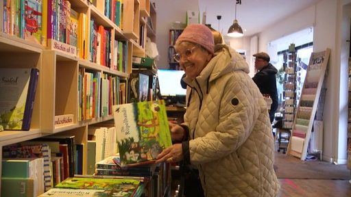 Eine ältere Dame schaut sich ein Kinderbuch im Buchladen an. 