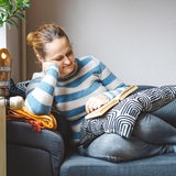 Eine Frau liest lächelnd auf dem Sofa ein Buch.