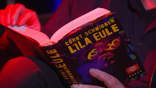 Der Roman "Lila Eule" von Cordt Schnibben wird aufgeschlagen in der Hand gehalten 