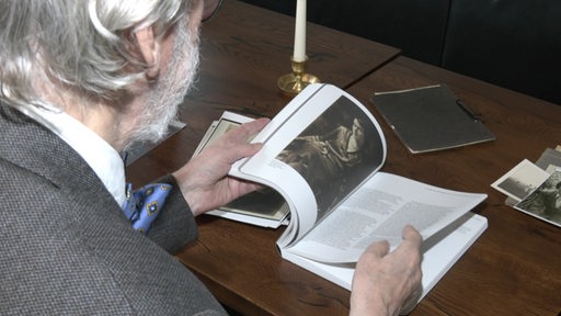 Ein älterer Mann sitzt an einem Tisch und blättert in einem Buch