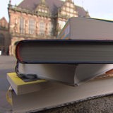 Im Vordergrund sind Bücher gestapelt, im Hintergrund der Bremer Marktplatz zu sehen.