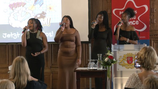 Vier junge Menschen stehen singen auf einer Bühne bei einer Preisverleihung.