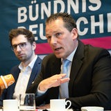 Jan Timke sitzt an einem Tisch mit Mikrofon, neben ihm Niklas Stadelmann und Piet Leidreiter 