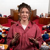 Eine Frau mit braunen Haaren gestikuliert vor der Kamera.