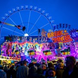 Das Fahrgeschäft Breakdancer ist auf dem Bremer Freimarkt hell beleuchtet. Es ist dunkel, Menschenmassen ziehen vor den Fahrgeschäften entlang.