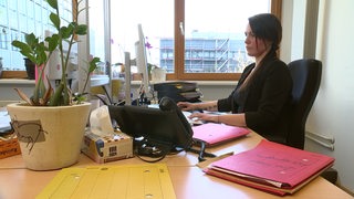 Eine Frau sitzt an einem Schreibtisch und arbeitet am Computer.