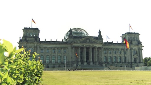 Das Bundestagsgebäude in Berlin. Es wehen mehrere Deutschlandfahnen im Wind.