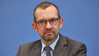 Politiker Thomas Röwekamp sitzt vor einem blauen Hintergrund