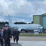 Mehrere uniformierte Personen laufen vor einem Flugzeug und einer Halle entlang.