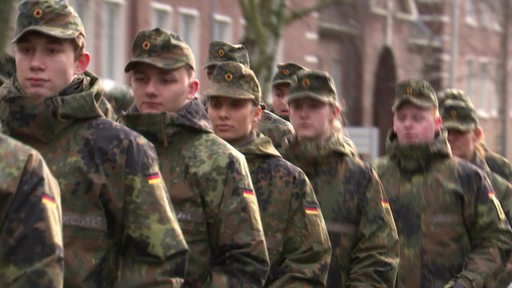 Frauen und Männer der Bundeswehr marschieren hintereinander her.