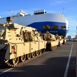 Panzer stehen auf einer Kaje. Im Hintergrund ist ein Schiff zu sehen.