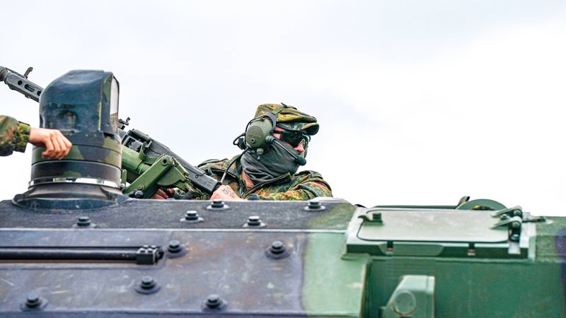 Ein Soldat schaut oben aus der Öffnung eines Panzers, an der linken Seite des Bildes ist eine Hand zu sehen.