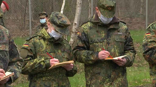 Es sind ein paar Bundeswehrsoldaten zu sehen, welche sich mit einem Stift etwas auf einem Zettel notieren.