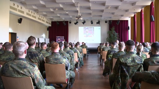 Mehrere Bundeswehrsoldat:innen sitzen, bei einer Aufklärungsveranstaltung über Depression, in einem großen Saal. 