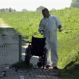 Mann im weißen Overall steht mit einer Messlatte neben einem Rollstuhl